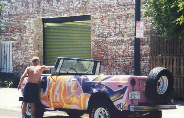 British street artist painting a vintage jeep in front of Sushi Performance and Visual Art in San Diego